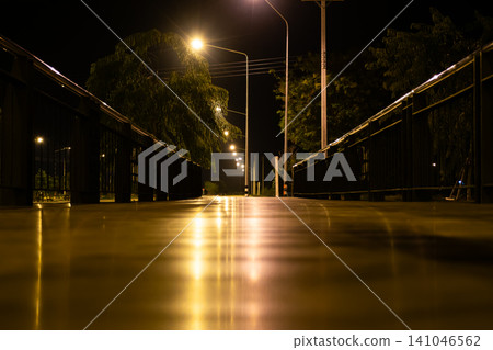 Illuminated pedestrian bridge at night glowing streetlights reflective surface strong perspective urban architecture peaceful evening atmosphere Illuminated pedestrian bridge at night glowing streetlights reflective surface strong perspective urban architecture peaceful evening atmosphere 141046562