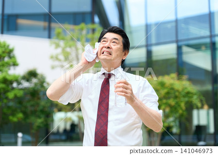 一位商人正在炎熱的戶外擦拭額頭的汗水。 141046973