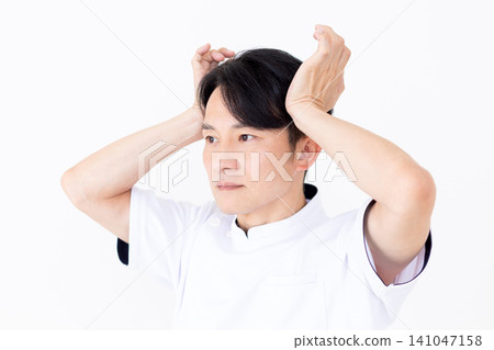 A middle-aged male acupuncturist/osteopath in a white coat presses on acupressure points on the temples (temporalis muscle). 141047158