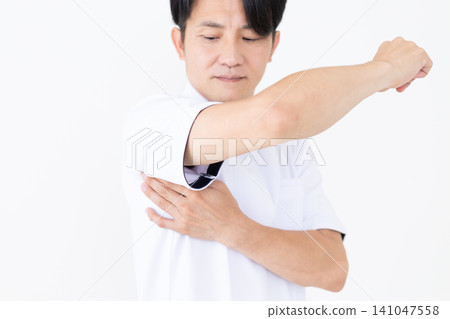 A middle-aged male acupuncturist/osteopath in a white coat presses on an acupressure point (serratus anterior muscle) under the armpit that is effective for stiff shoulders. A middle-aged male acupuncturist/osteopath in a white coat presses on an acupressure point (serratus anterior muscle) under the armpit that is effective for stiff shoulders. 141047558