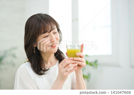 一位六十多歲的婦女在客廳喝蔬菜汁。 一位六十多歲的婦女在客廳喝蔬菜汁。 141047608