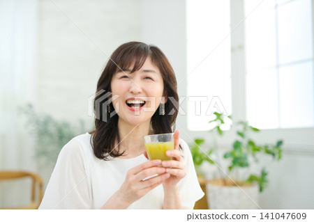 A woman in her 60s drinking vegetable juice in her living room. A woman in her 60s drinking vegetable juice in her living room. 141047609