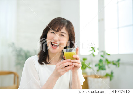 一位六十多歲的婦女在客廳喝蔬菜汁。 一位六十多歲的婦女在客廳喝蔬菜汁。 141047610
