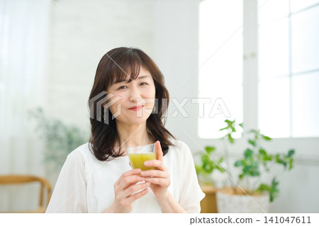 A woman in her 60s drinking vegetable juice in her living room. A woman in her 60s drinking vegetable juice in her living room. 141047611