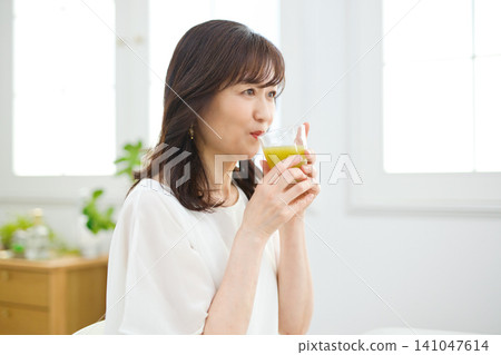 A woman in her 60s drinking vegetable juice in her living room. A woman in her 60s drinking vegetable juice in her living room. 141047614