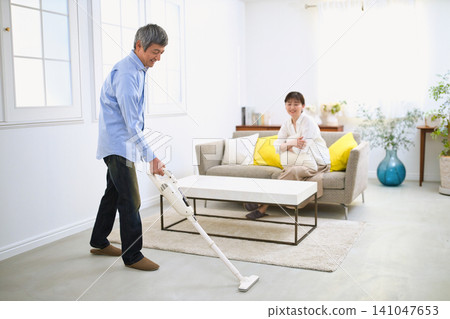 A smiling man and a woman in her 60s vacuum while chatting. 141047653