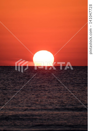 美麗的圓形日落(歐米伽太陽)沉入地平線以下,天空被染成深紅色(垂直構圖)。 美麗的圓形日落(歐米伽太陽)沉入地平線以下,天空被染成深紅色(垂直構圖)。 141047728