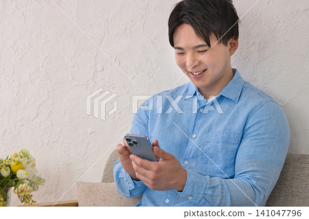 A young man relaxing on a sofa while looking at his smartphone 141047796