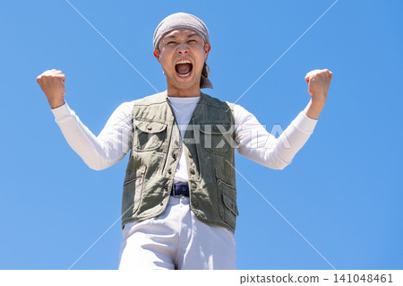 一名身穿工作服的男子在藍天下擺出勝利姿勢。 一名身穿工作服的男子在藍天下擺出勝利姿勢。 141048461