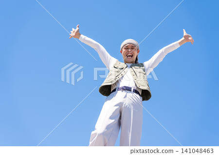 一名身穿工作服的男子在藍天下高舉雙臂歡呼。 一名身穿工作服的男子在藍天下高舉雙臂歡呼。 141048463