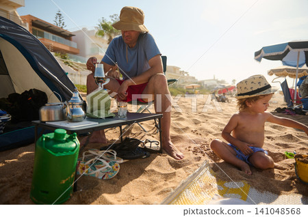 Father and toddler on sandy beach camping at sunrise enjoying family holiday and seaside play Father and toddler on sandy beach camping at sunrise enjoying family holiday and seaside play 141048568