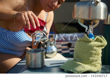 Woman preparing loose leaf tea at campsite with portable stove and stainless teapot Woman preparing loose leaf tea at campsite with portable stove and stainless teapot 141048717