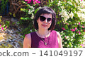 Woman in sunglasses and cherry-red dress standing in bright summer sunlight 141049197