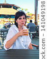 Heat-weary woman sitting in a shaded cafe, sipping a glass of cold juice on a hot summer day 141049198