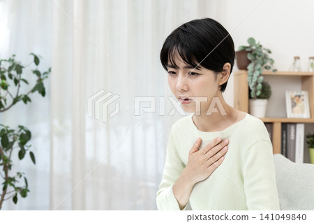 一位年輕女子摀著胸口，因反流性食道炎而感到胃灼熱和噁心。 141049840