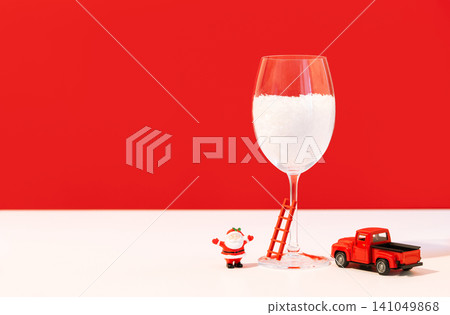 Miniature Santa figurine climbing a small ladder leaning against a snow-filled wine glass Miniature Santa figurine climbing a small ladder leaning against a snow-filled wine glass 141049868