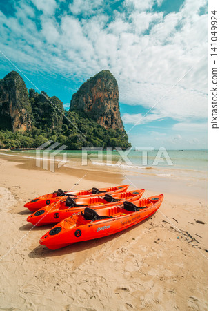 Three bright orange kayaks on a tropical sandy beach with majestic limestone cliffs in Krabi, Thailand. Three bright orange kayaks on a tropical sandy beach with majestic limestone cliffs in Krabi, Thailand. 141049924