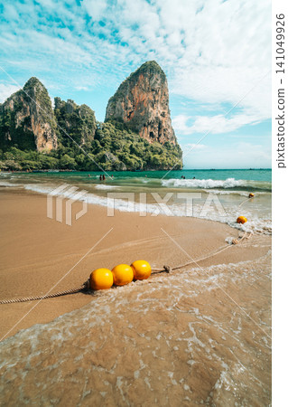 Scenic tropical beach with yellow buoys in the water and towering limestone cliffs in Scenic tropical beach with yellow buoys in the water and towering limestone cliffs in 141049926