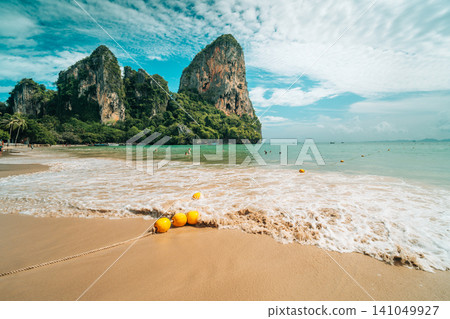 Scenic tropical beach with yellow buoys in the water and towering limestone cliffs in Scenic tropical beach with yellow buoys in the water and towering limestone cliffs in 141049927