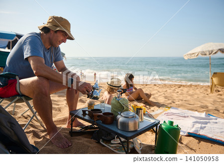 Father making tea on the beach while family relaxes on a sunny summer day 141050958
