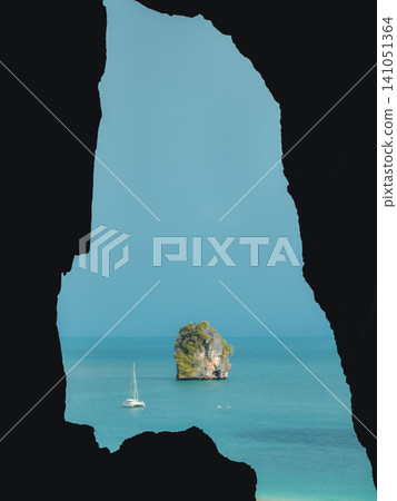 Silhouette of a dark cave framing a stunning view of a sailboat in the tropical turquoise ocean. Silhouette of a dark cave framing a stunning view of a sailboat in the tropical turquoise ocean. 141051364