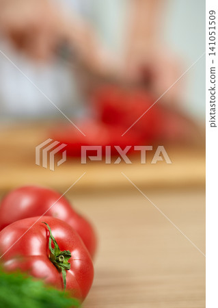 Chef's hands chopping organic ripe red tomatoes on a wooden cutting board, preparing healthy food ingredients Chef's hands chopping organic ripe red tomatoes on a wooden cutting board, preparing healthy food ingredients 141051509