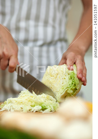Hands holding a sharp knife and cutting a head of green cabbage into thin shreds for healthy meal preparation 141051597