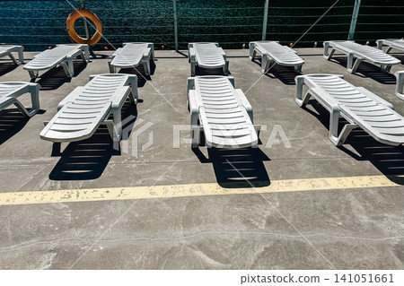 Empty sun loungers on a sunny deck by the water in a relaxing vacation setting Empty sun loungers on a sunny deck by the water in a relaxing vacation setting 141051661