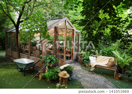 Beautiful greenhouse surrounded by lush greenery in a peaceful garden setting 141051669