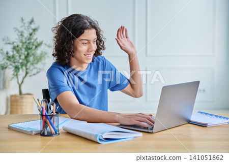 Happy teenage boy waving hand at laptop on desk 141051862