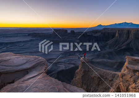 Adventurer expresses joy standing atop majestic cliff overlooking vast desert landscape of utah during breathtaking sunset. rugged canyon stretches into distance Adventurer expresses joy standing atop majestic cliff overlooking vast desert landscape of utah during breathtaking sunset. rugged canyon stretches into distance 141051968