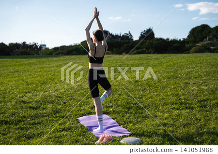 Practicing balancing yoga poses under a sunny sky in a green park 141051988