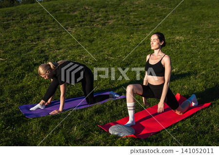 Women practicing yoga outdoors on a sunny afternoon in a green park Women practicing yoga outdoors on a sunny afternoon in a green park 141052011