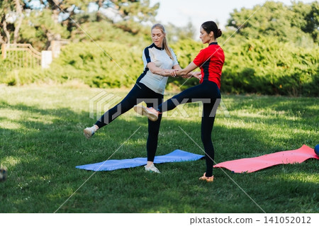 Two women practice yoga in the park on mats 141052012