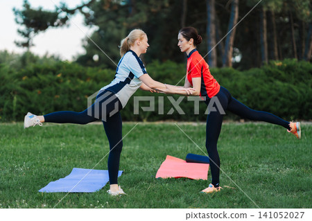 Women practice yoga together in a park setting Women practice yoga together in a park setting 141052027