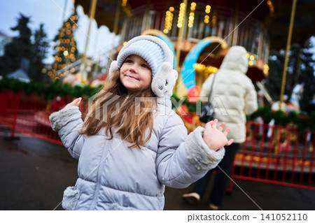 Joyful girl enjoying winter festivities at a carousel in the park Joyful girl enjoying winter festivities at a carousel in the park 141052110