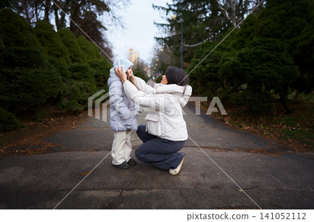 Mother adjusting childs hood in a serene outdoor setting on a cool day Mother adjusting childs hood in a serene outdoor setting on a cool day 141052112
