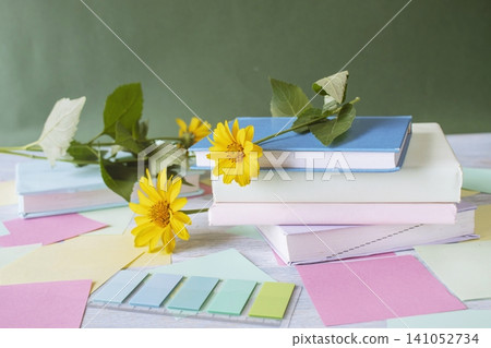Stack of books with yellow flower bookmarks, stickers on the table, on the background of the blackboard. Back to school concept. Stack of books with yellow flower bookmarks, stickers on the table, on the background of the blackboard. Back to school concept. 141052734
