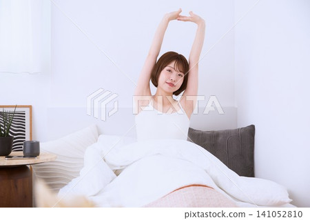 A smiling young woman stretching in bed in the morning. A smiling young woman stretching in bed in the morning. 141052810