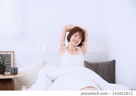 A young woman with a smile stretches in bed in the morning. A young woman with a smile stretches in bed in the morning. 141052812