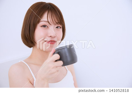 一位留著短髮的年輕女子手捧馬克杯,面帶微笑。 一位留著短髮的年輕女子手捧馬克杯,面帶微笑。 141052818
