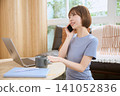 A young woman using a laptop while talking on her smartphone in her living room at home. 141052836