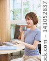 A smiling young woman drinking coffee while using her laptop in the living room. 141052837