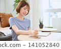 A young woman with bobbed hair and a smile is writing in a notebook in the living room. 141052840