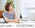 A young woman thinking while writing on a tablet with a pen in her living room. 141052841