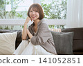 A young woman with bobbed hair sits on a sofa, relaxing and smiling. 141052851
