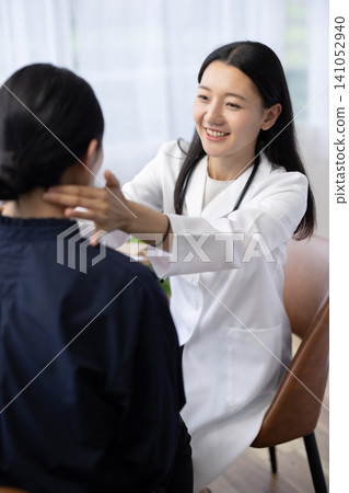 一位年輕的日本女醫生將手放在病人脖子上檢查。 141052940