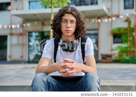 Smiling young student with glasses, headphones sitting outside Smiling young student with glasses, headphones sitting outside 141053131