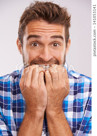 Nervous, portrait and man with nail bite for anxiety, fear and funny stress gesture in a studio. Worried, scared and male person with hands to face for comedy with grey background and modern style 141053141