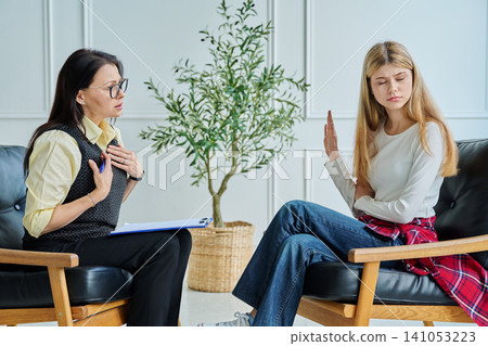 Rebellious teenage girl refusing to talk to female psychologist at therapy session Rebellious teenage girl refusing to talk to female psychologist at therapy session 141053223